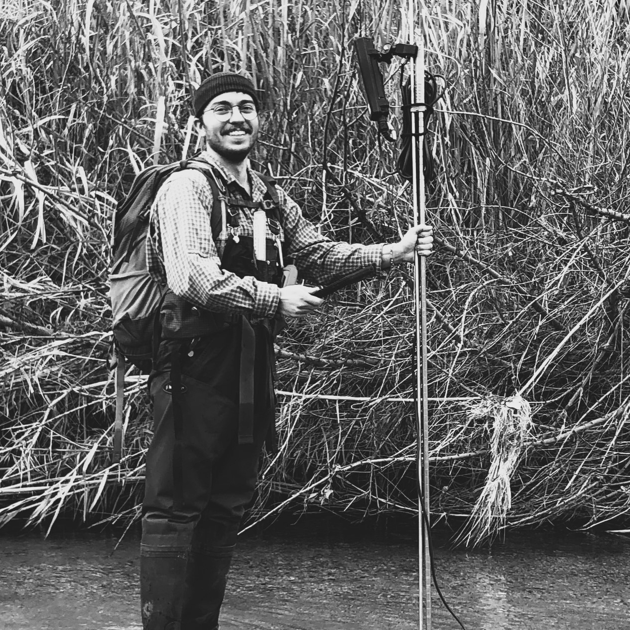 Field crew member Emerson Martin stands in a stream, holding water quality monitoring equipment.
